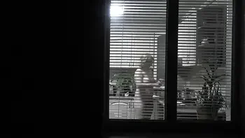 Peeping. Voyeur. Neighbor pervert voyeur in evening on street looks out window as naked sexy neighbor in kitchen prepares dinner for her husband. Naked in public. Naked at home. Family.  Outdoor